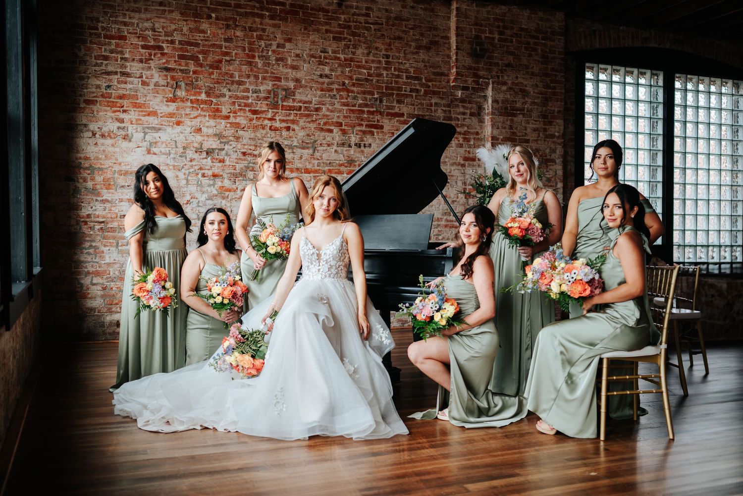 Wedding party in sage green dresses seated on vintage furniture in an industrial brick venue.