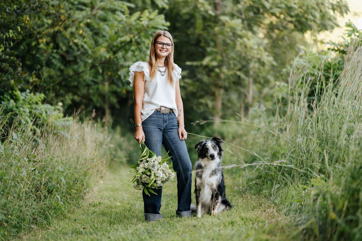 A dog walks alongside its owners on a nature trail surrounded by lush greenery.