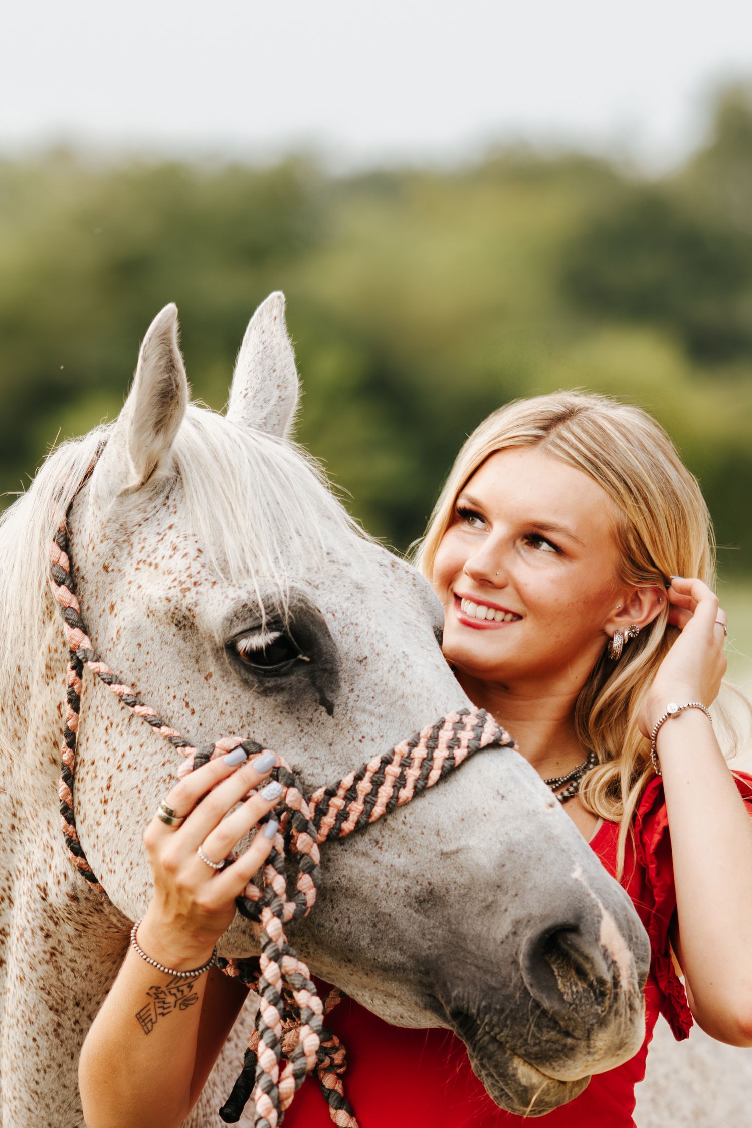 A person in red shares tender moments with a white horse in a sunlit field.