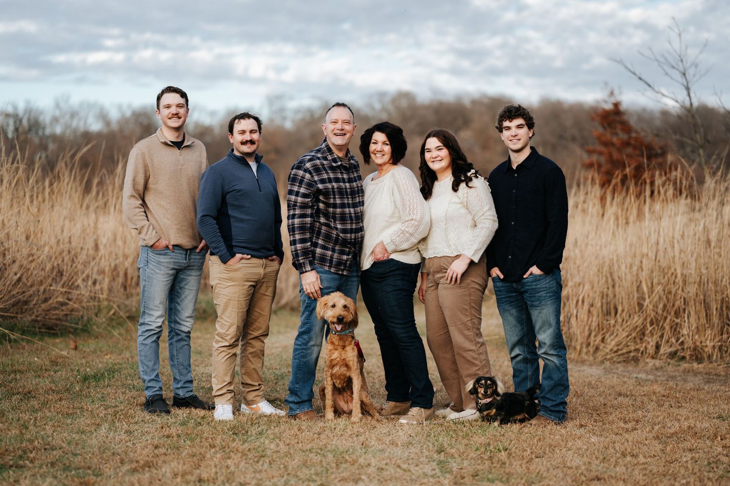 A group poses together in autumn field with tall golden grass during outdoor family photo session.