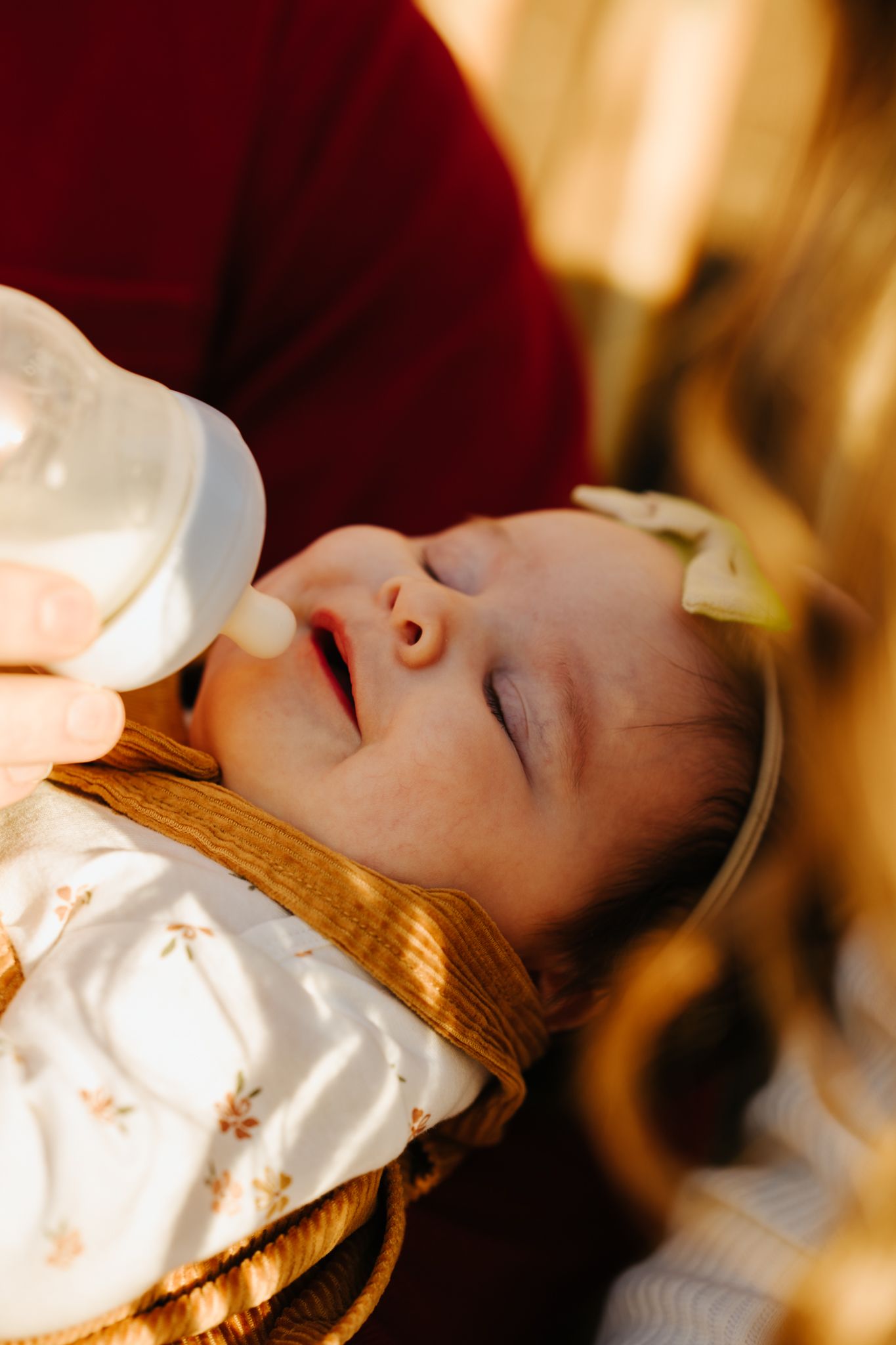 A peaceful sleeping baby in white clothing drinks from a bottle while resting on a golden surface.