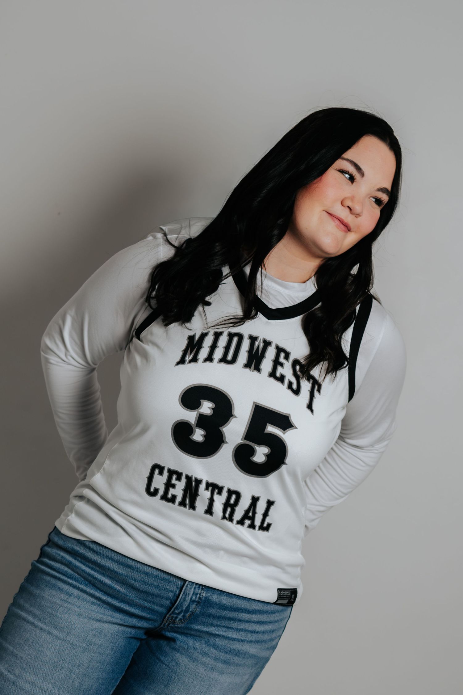 Studio portraits in white Midwest Central sports jersey and jeans against grey background.