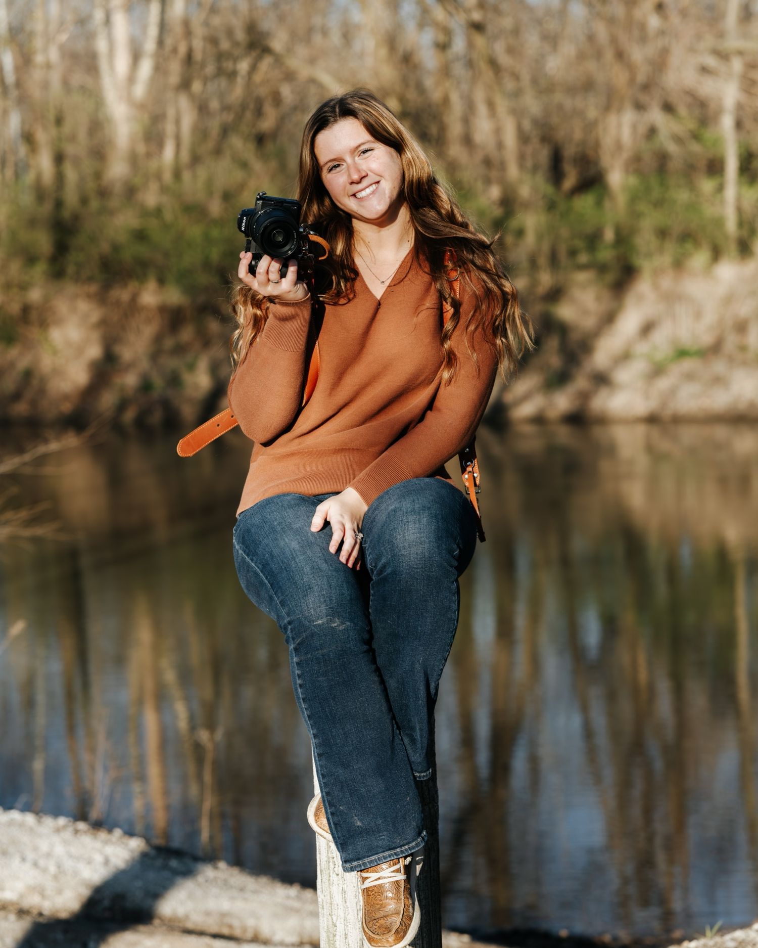 Person in brown sweater sitting by lake during golden hour.