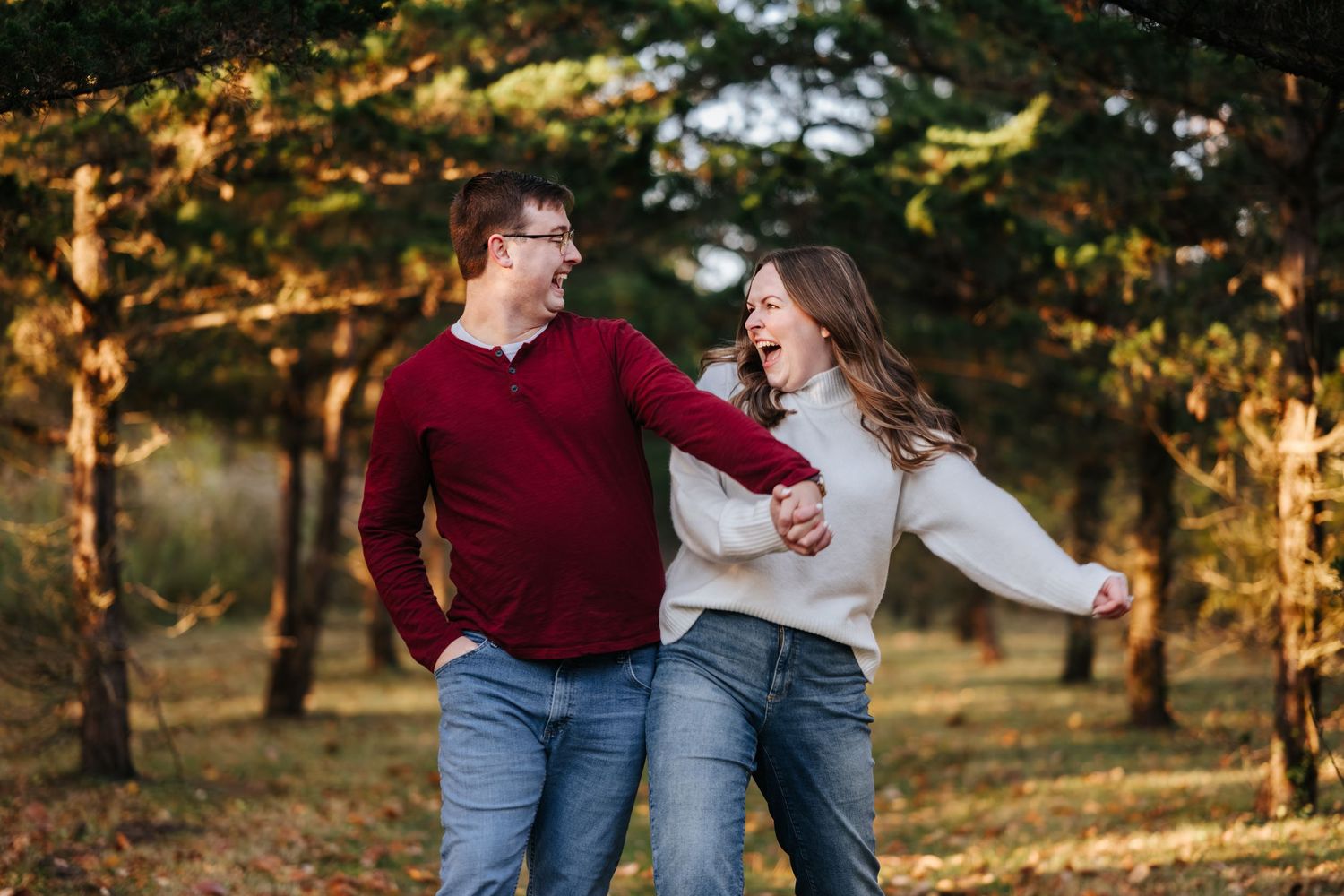 Couple in casual attire laughs together in a sunlit outdoor setting.