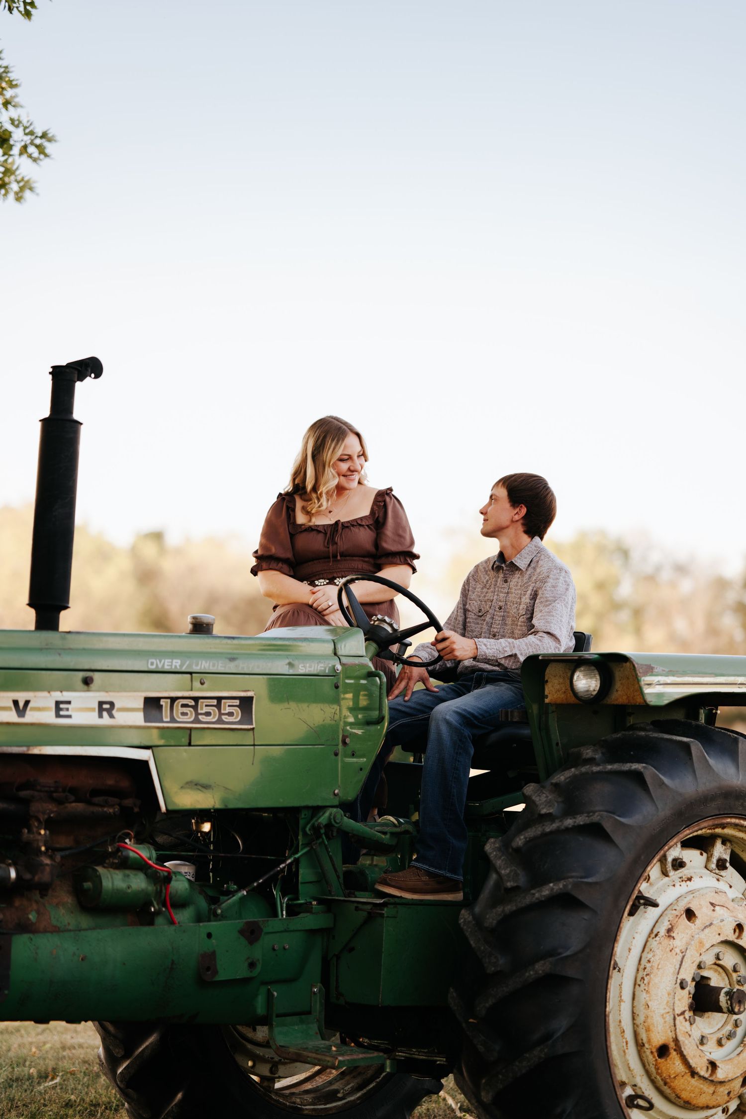 Couple poses on vintage green John Deere tractor during rustic outdoor photoshoot.
