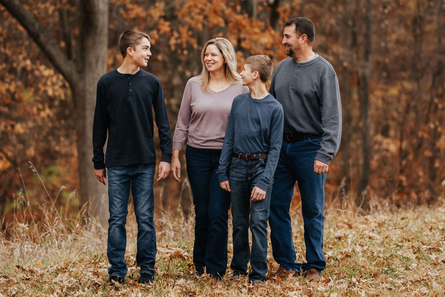 A family walks together through a forest with golden autumn foliage in the background.