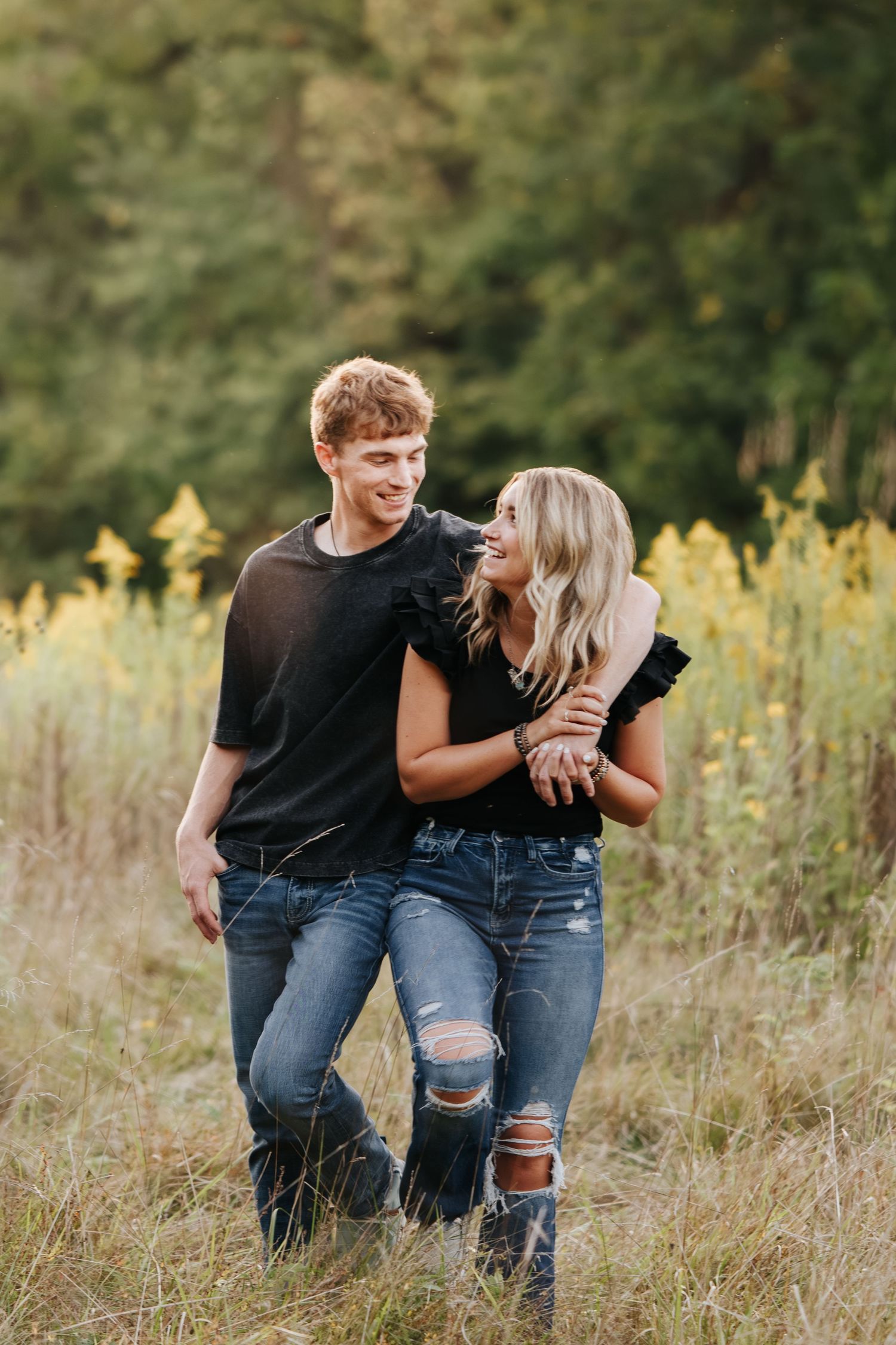 Couple in casual wear laughing together in tall grass field.
