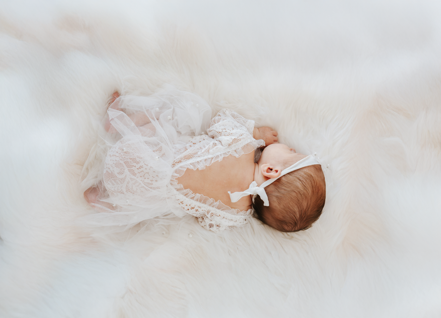 Delicate newborn baby lying on soft white fabric in a dreamy, ethereal setting.