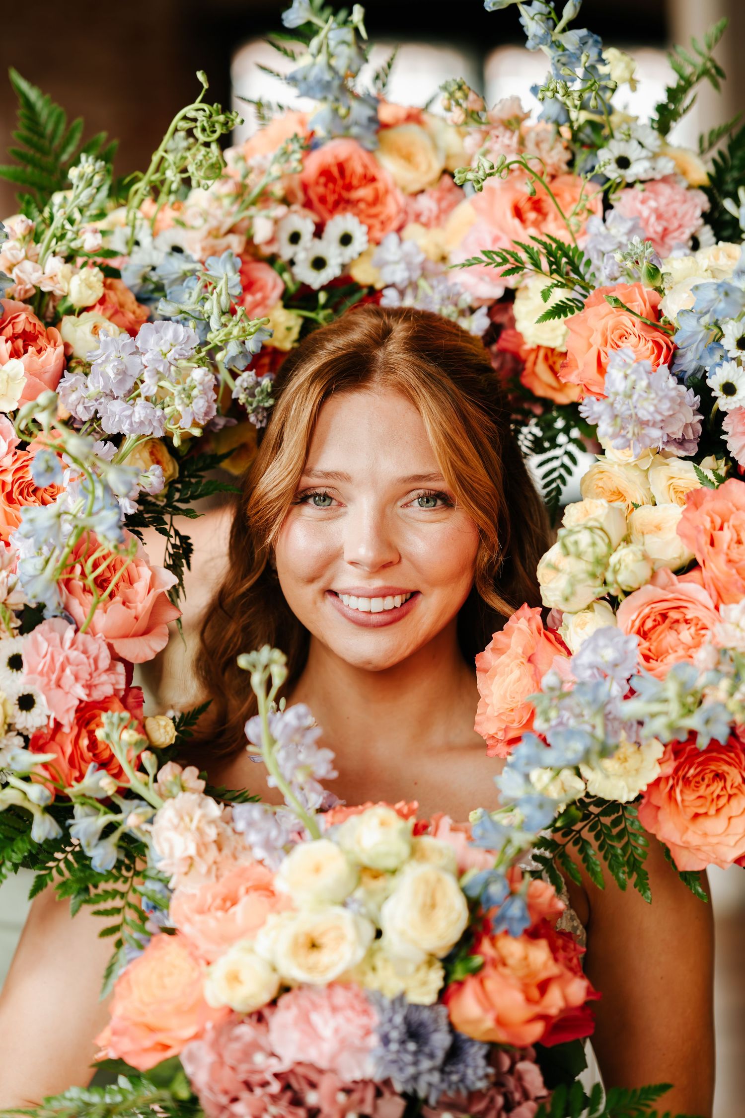 Colorful floral arrangement with coral roses, white flowers, and blue hydrangeas framing a dreamy portrait.