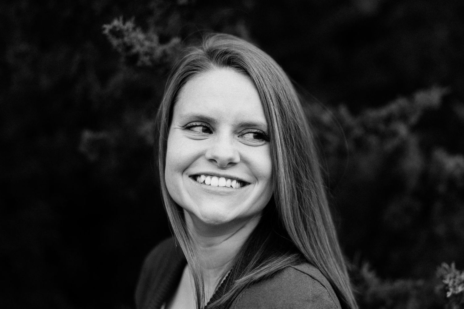Black and white outdoor portrait showing a joyful expression and long straight hair.