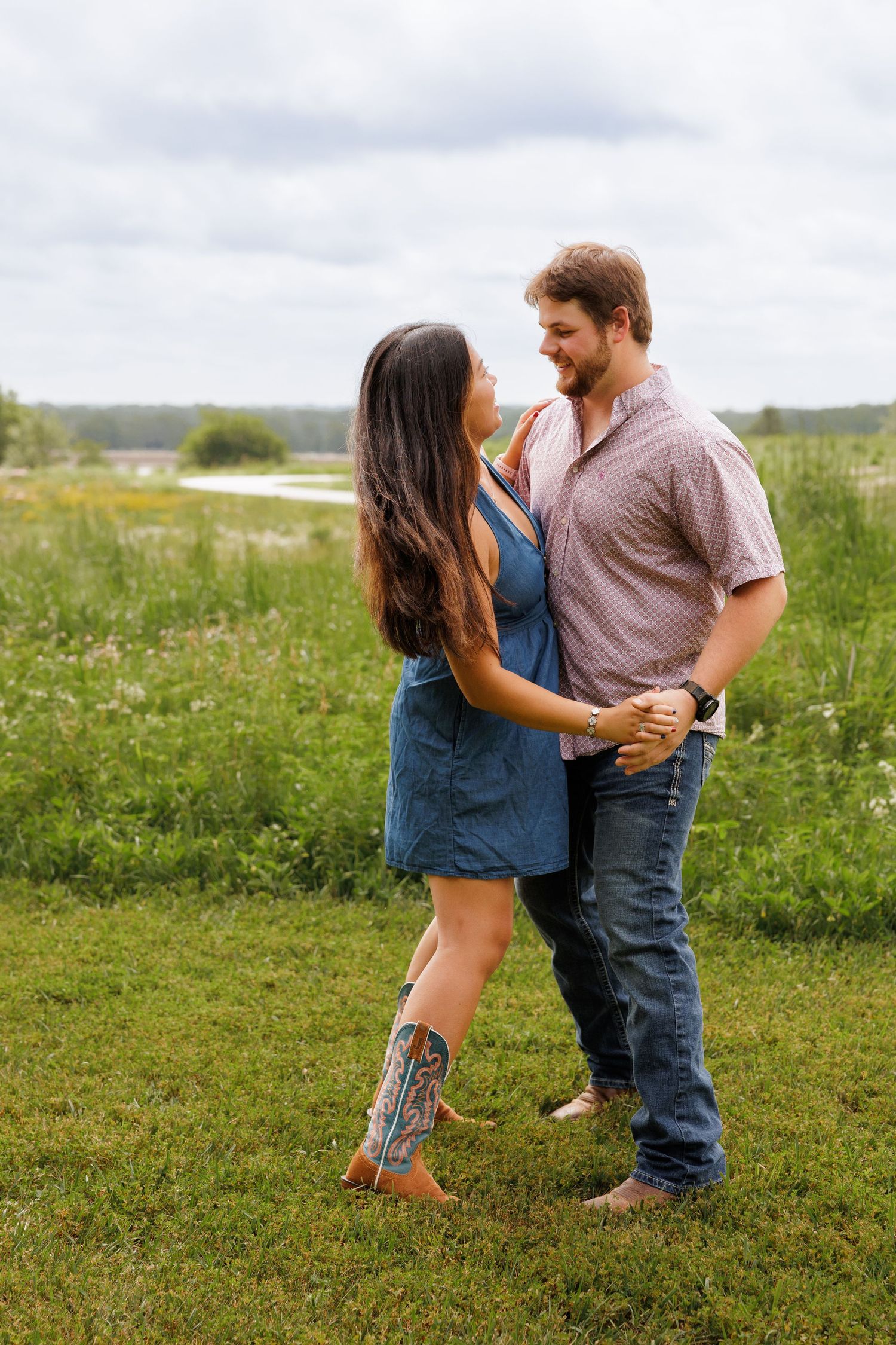 Couple dancing together in a green meadow, woman in denim dress with cowboy boots, man in plaid shirt and jeans.