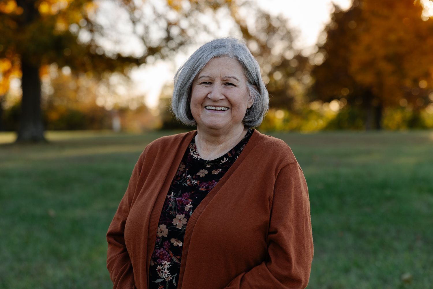Person in brown cardigan smiling outdoors during golden hour sunset.