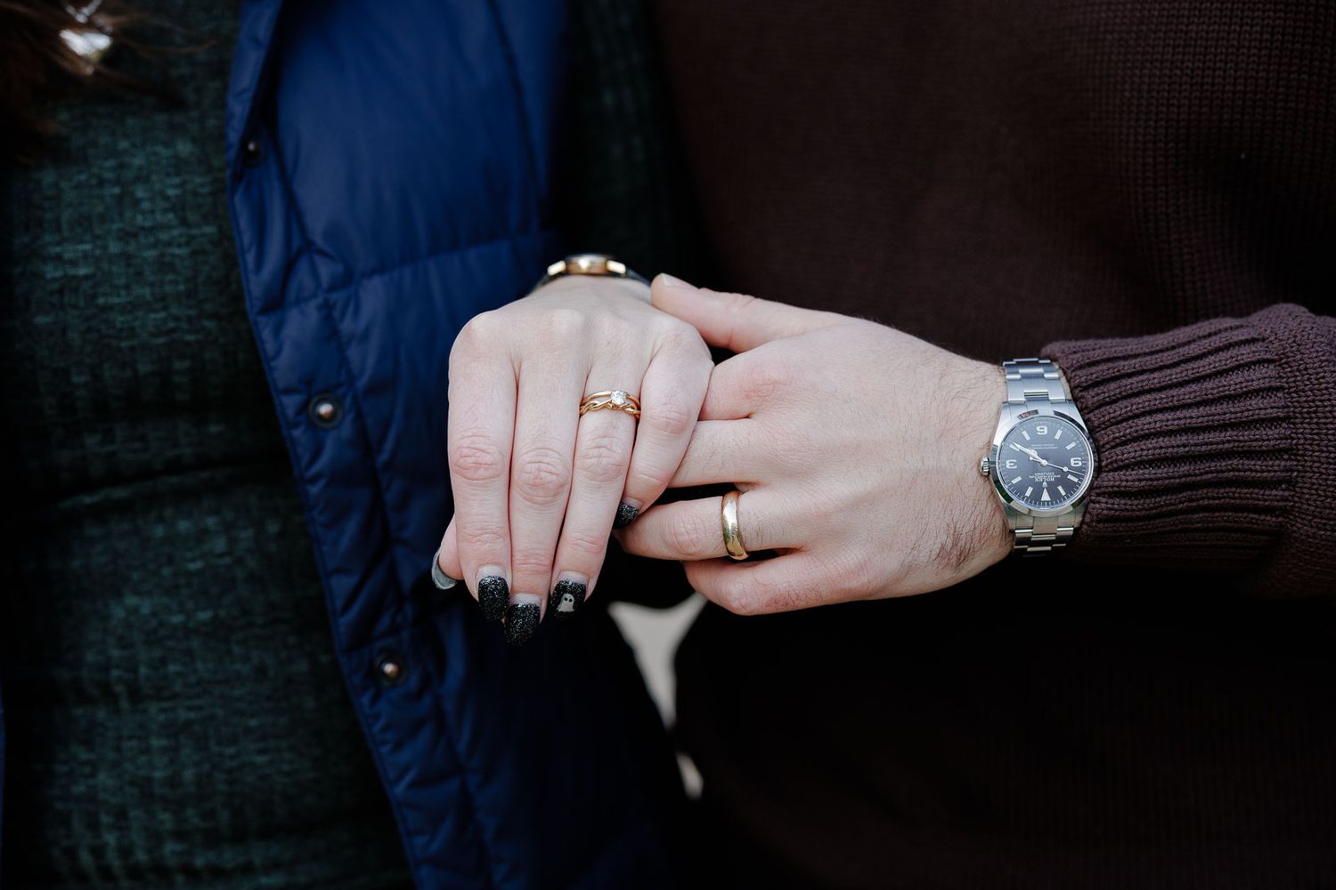 Close-up of hands showing engagement rings and a watch against dark clothing.