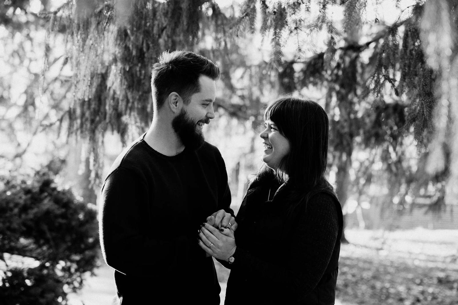 A romantic black and white portrait of a couple sharing an intimate moment outdoors under trees.