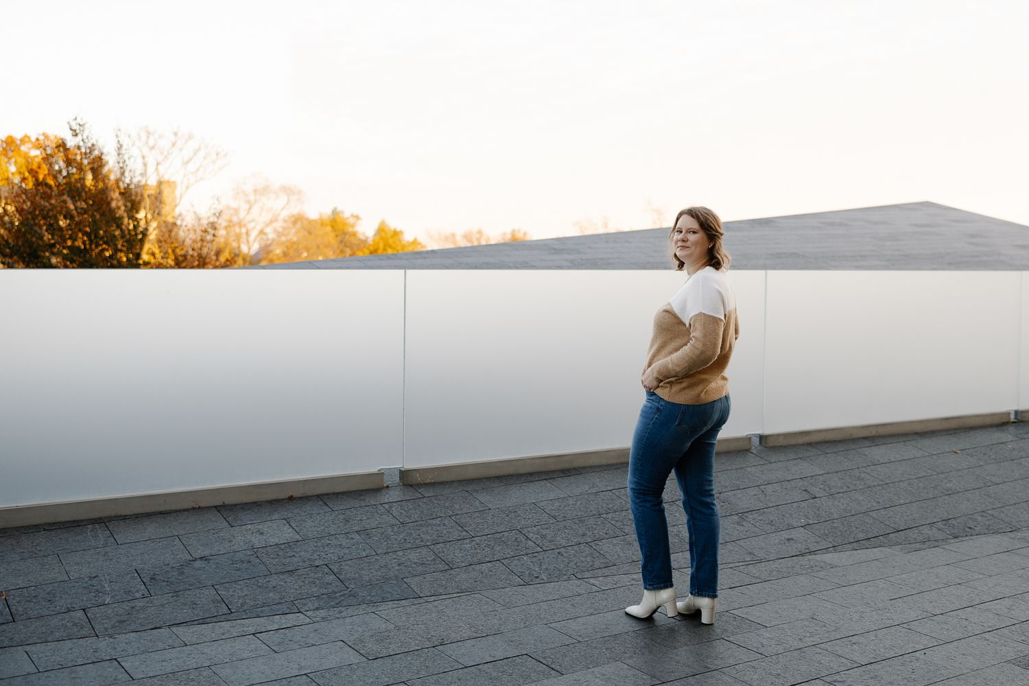 Woman in jeans and boots walking along a concrete path during golden hour sunset.