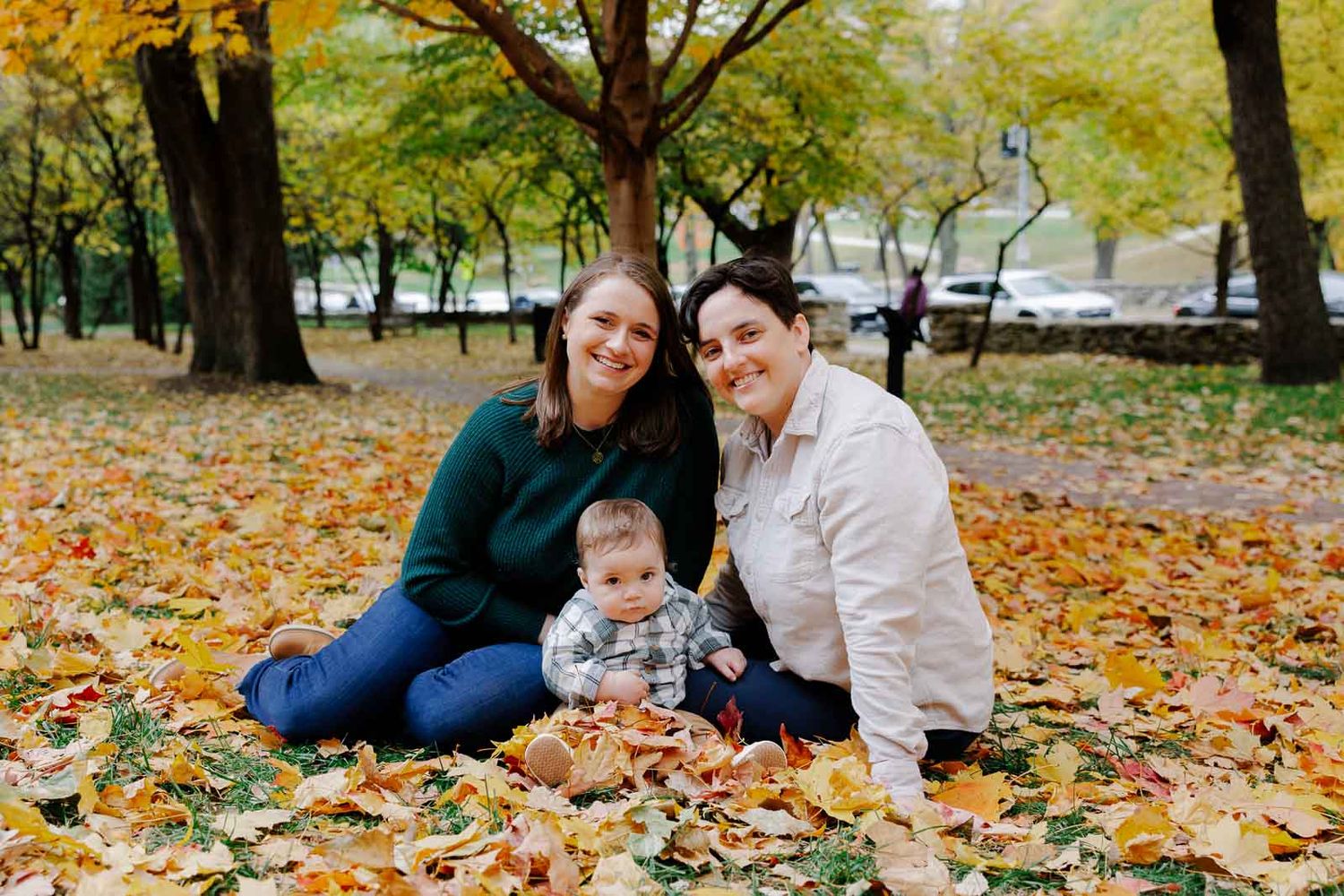 A family sits together on fallen autumn leaves in a park on a crisp fall day.
