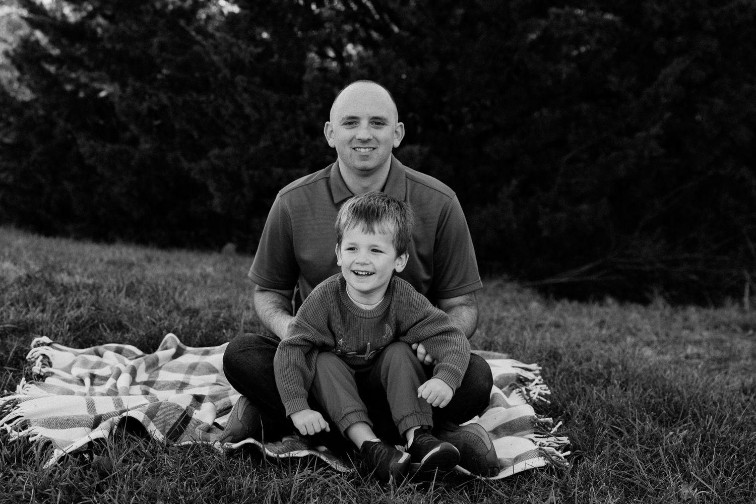 Black and white photo of two people sitting together on a blanket outdoors.
