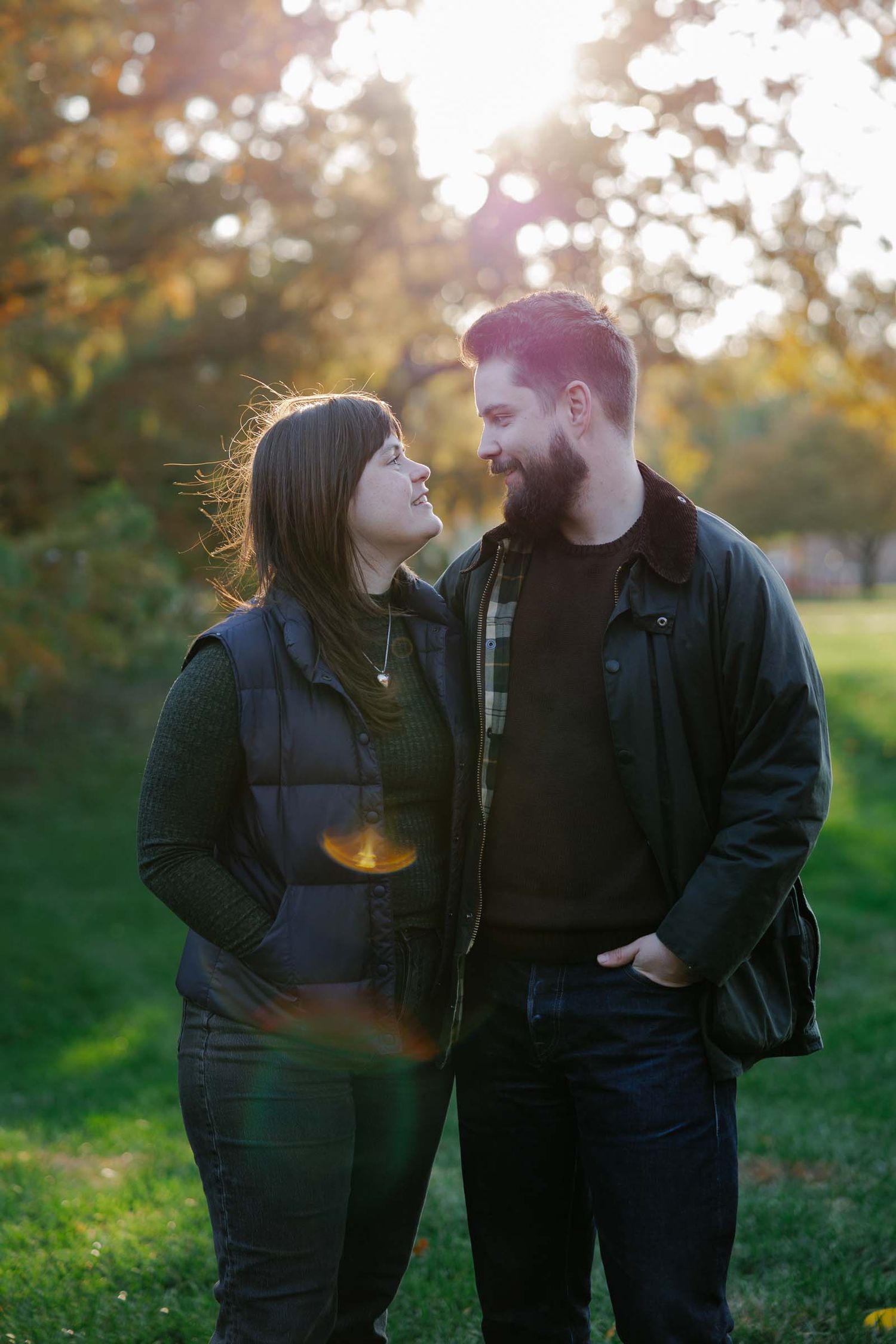 A couple shares a tender moment together outdoors during golden hour with autumn foliage in the background.