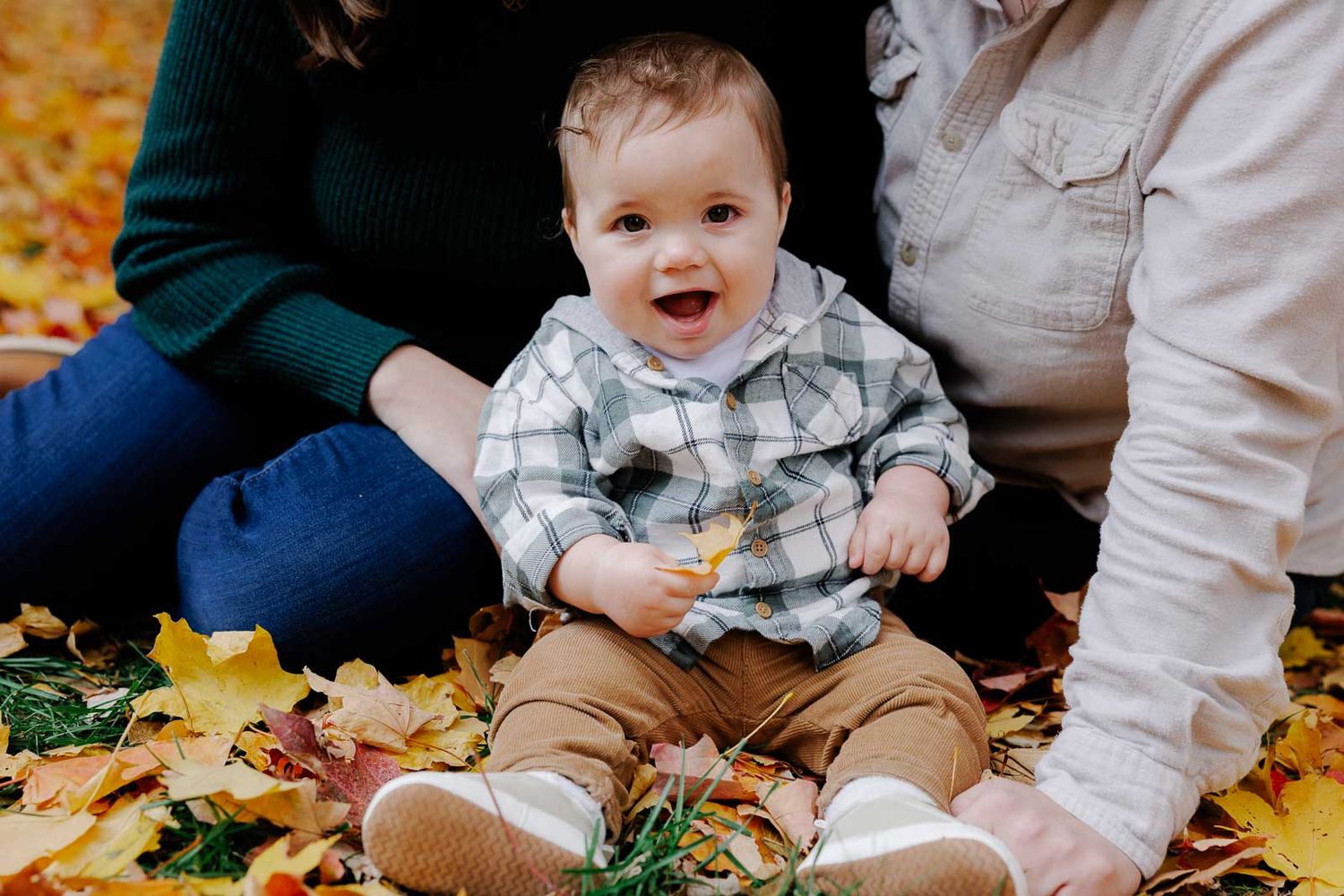 Happy baby laughing while being held by parents during fall photoshoot.