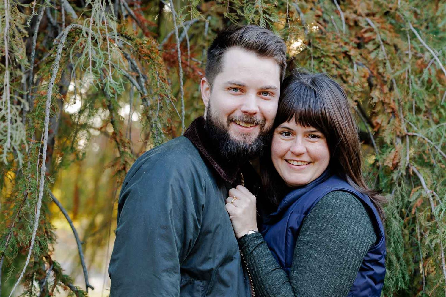 A happy couple poses together outdoors surrounded by autumn foliage and natural lighting.