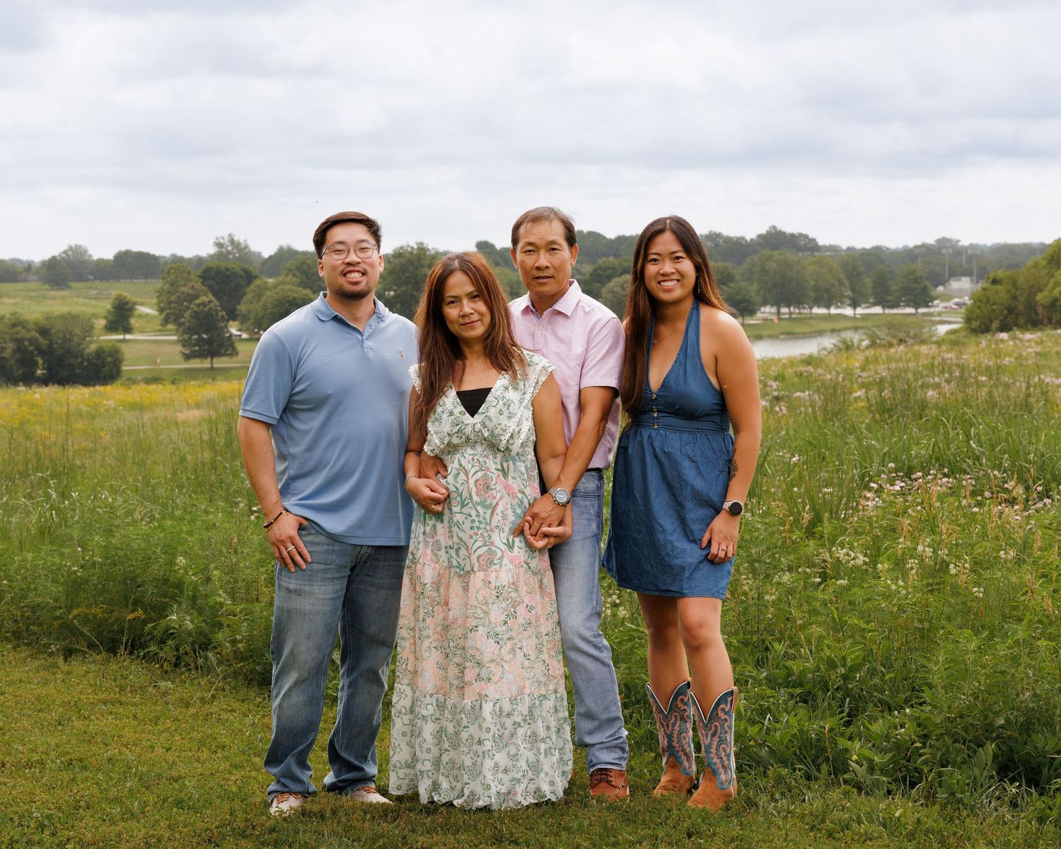 Asian family of four smiling together in a scenic wildflower meadow on a cloudy day.