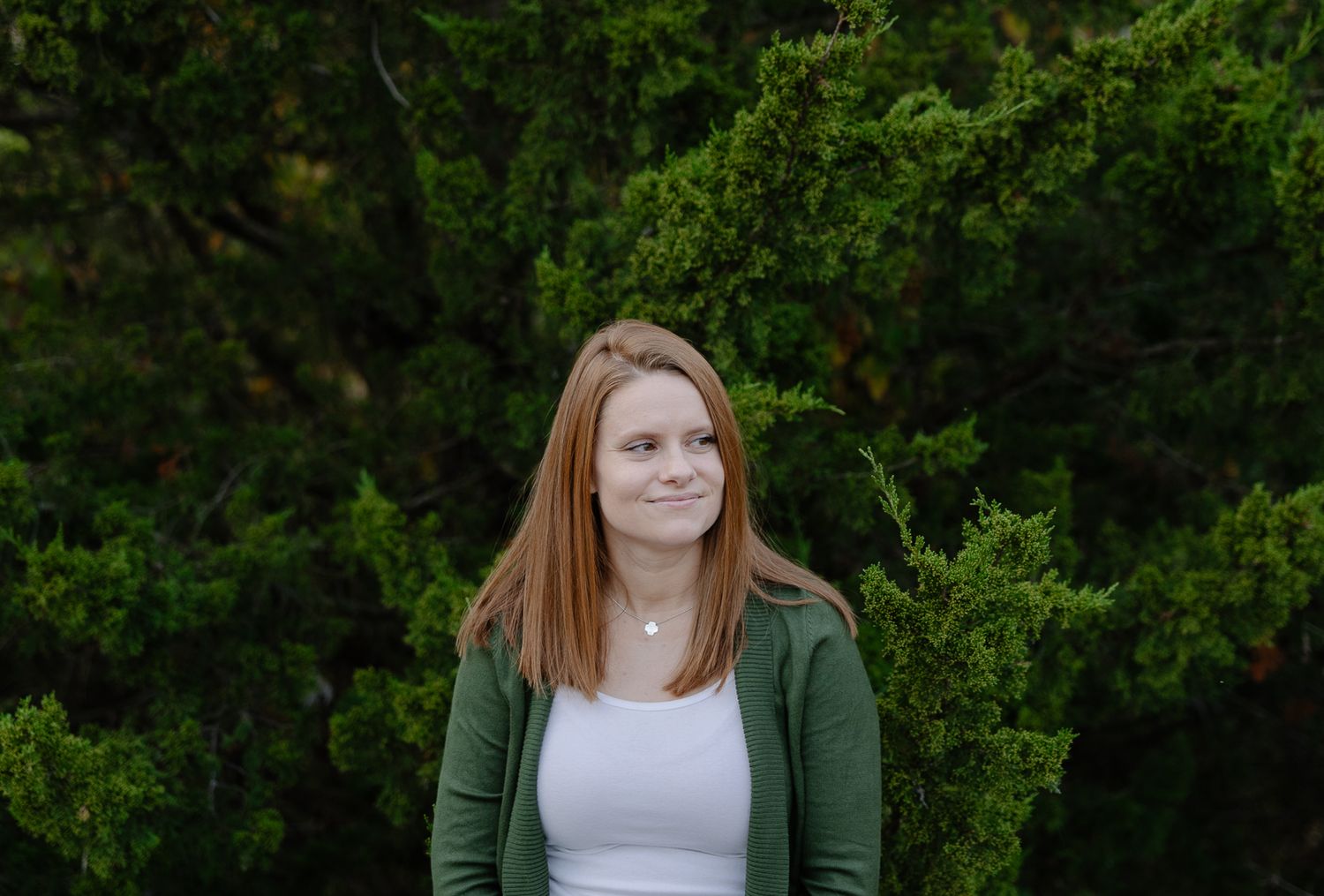 Casual outdoor portrait with someone wearing a white top and green cardigan against foliage.