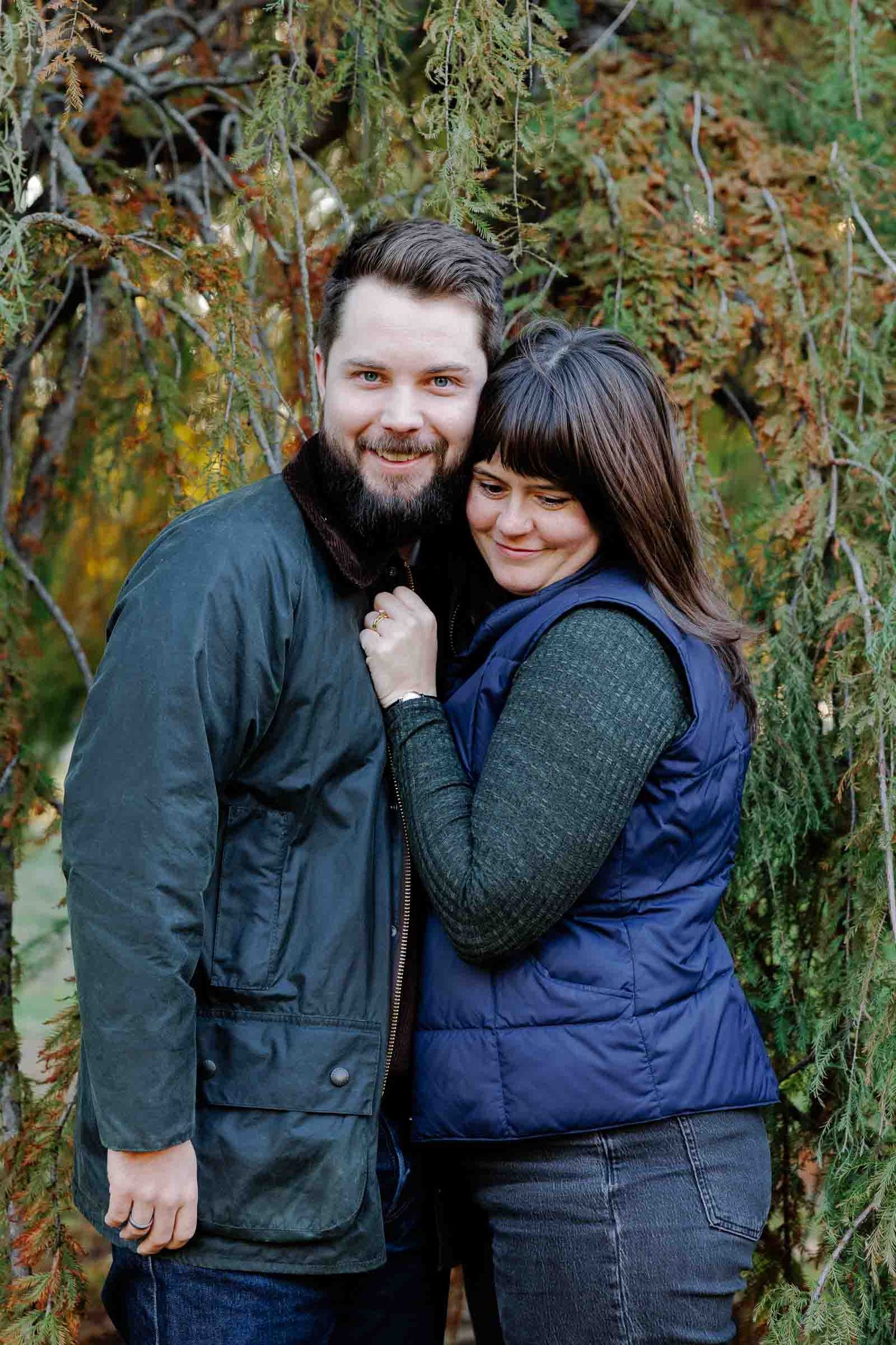 Couple in warm clothing embracing and laughing together among autumn foliage.