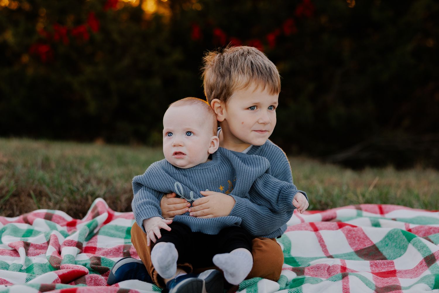 Two young children sitting together on a plaid picnic blanket at sunset.