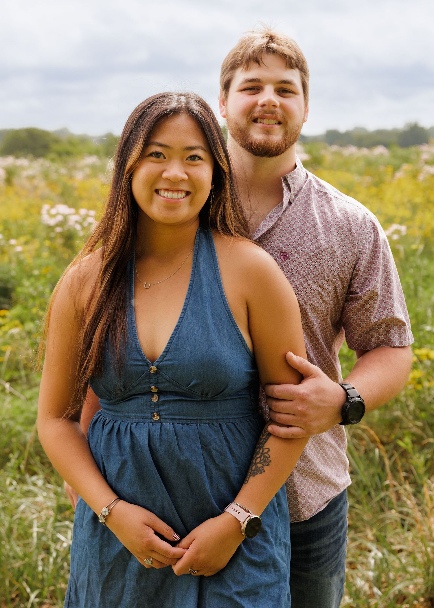 Smiling young couple posing together in a colorful wildflower field on an overcast day.