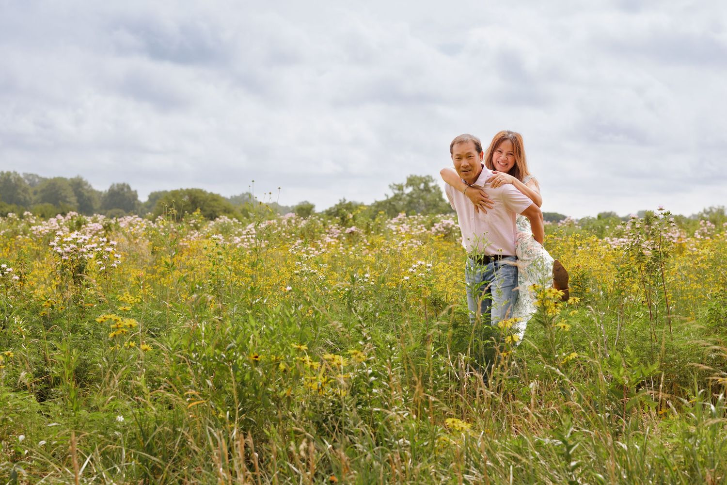 Couple sharing a piggyback ride in a vibrant wildflower meadow under cloudy skies.