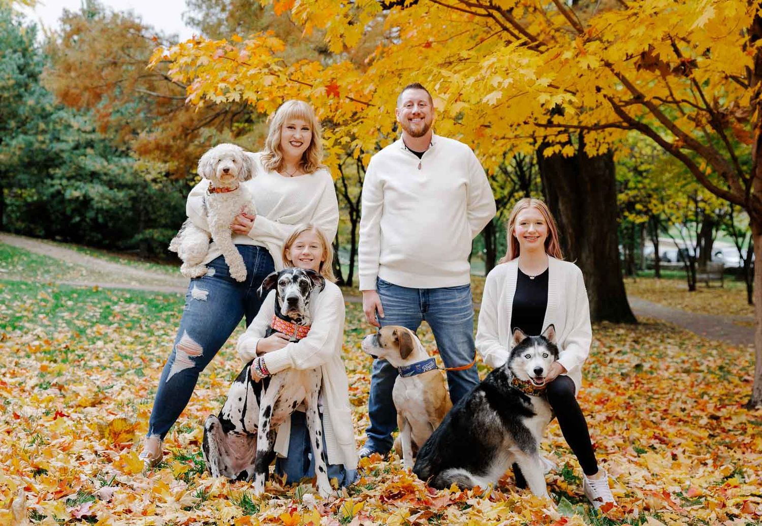 Family with dogs posing together for a portrait amid vibrant fall foliage.