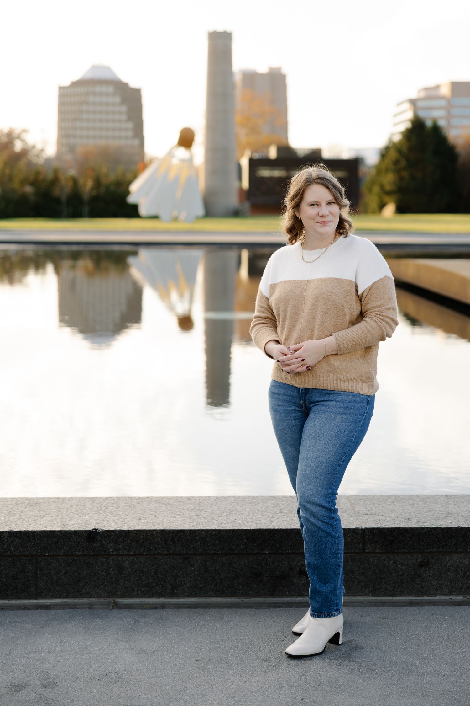A casual autumn portrait by a reflective pool with modern buildings and architecture in the background.