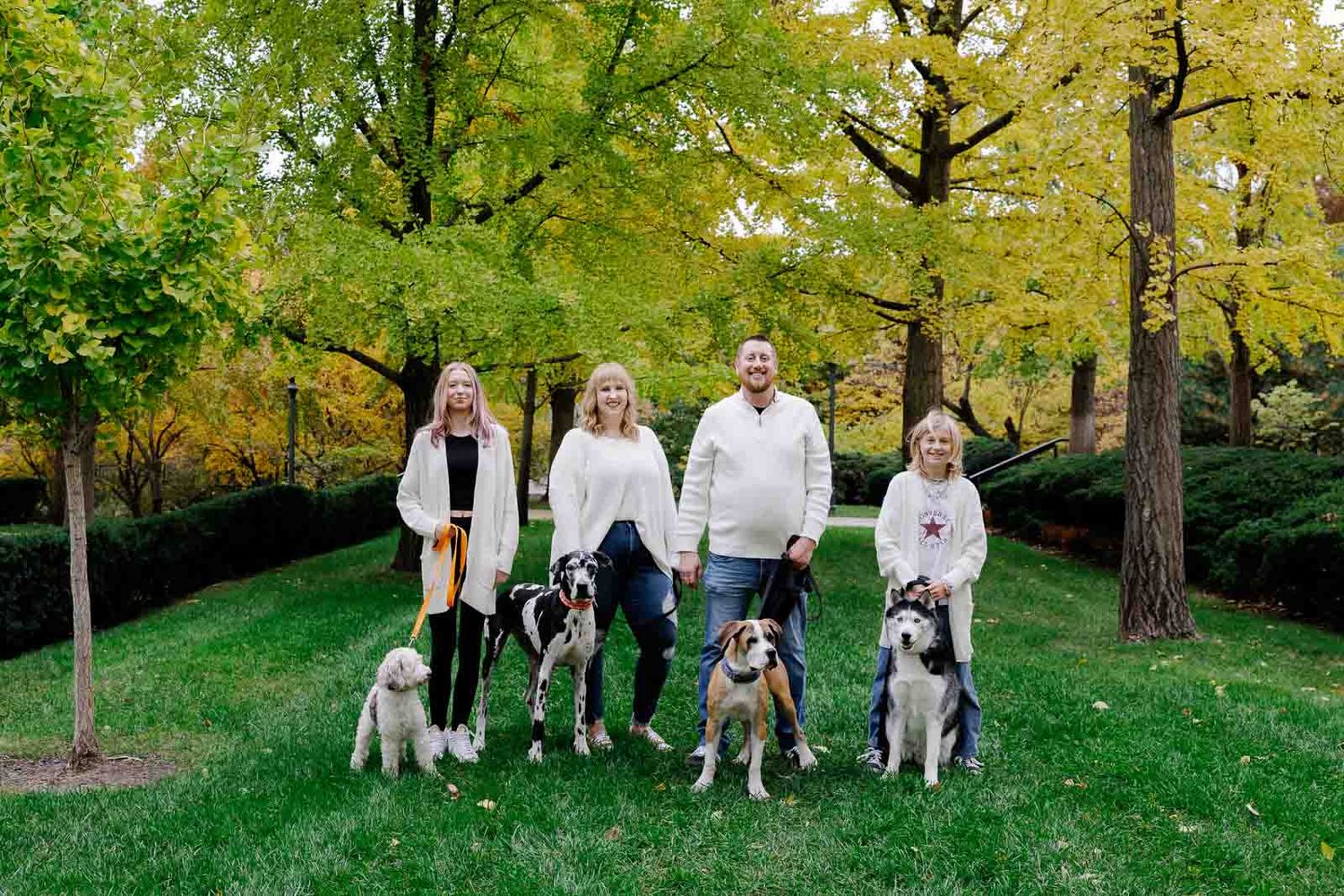Family group portrait with multiple dogs standing together under autumn trees.