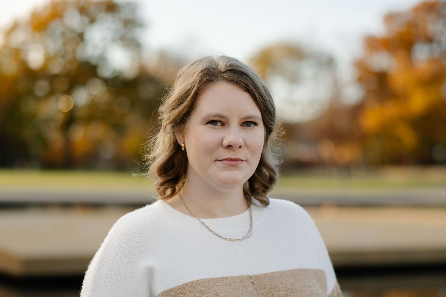 A person in a white and beige color block sweater poses outdoors during an autumn photoshoot.