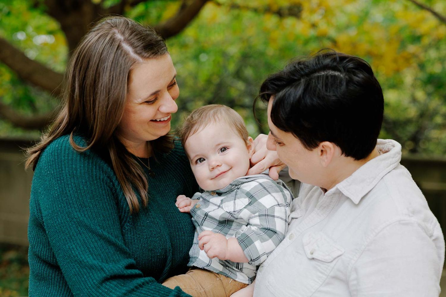 Family portrait session in autumn with parents and baby sitting among fallen leaves.