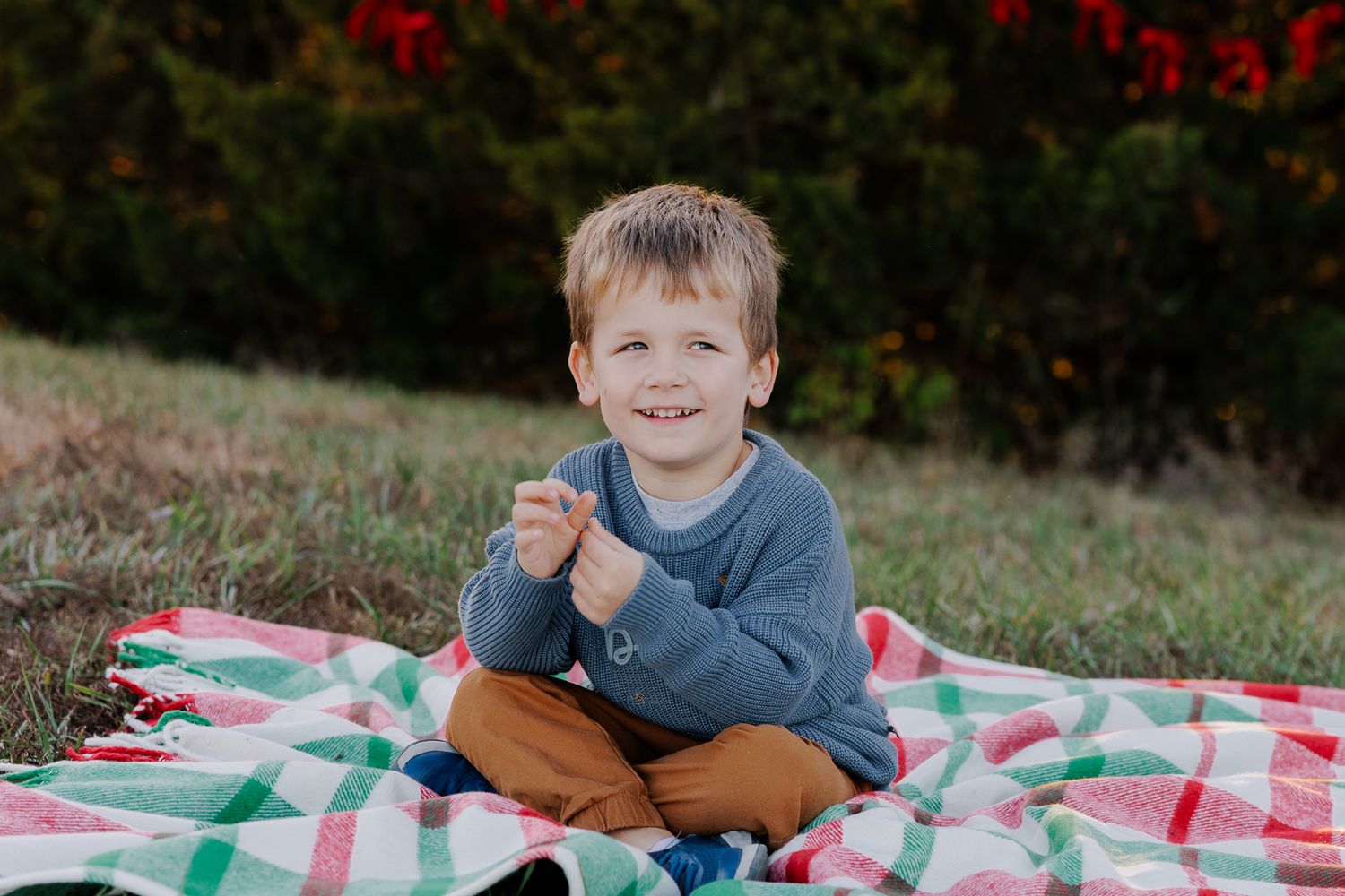 Young child sitting cross-legged on a plaid blanket outdoors.