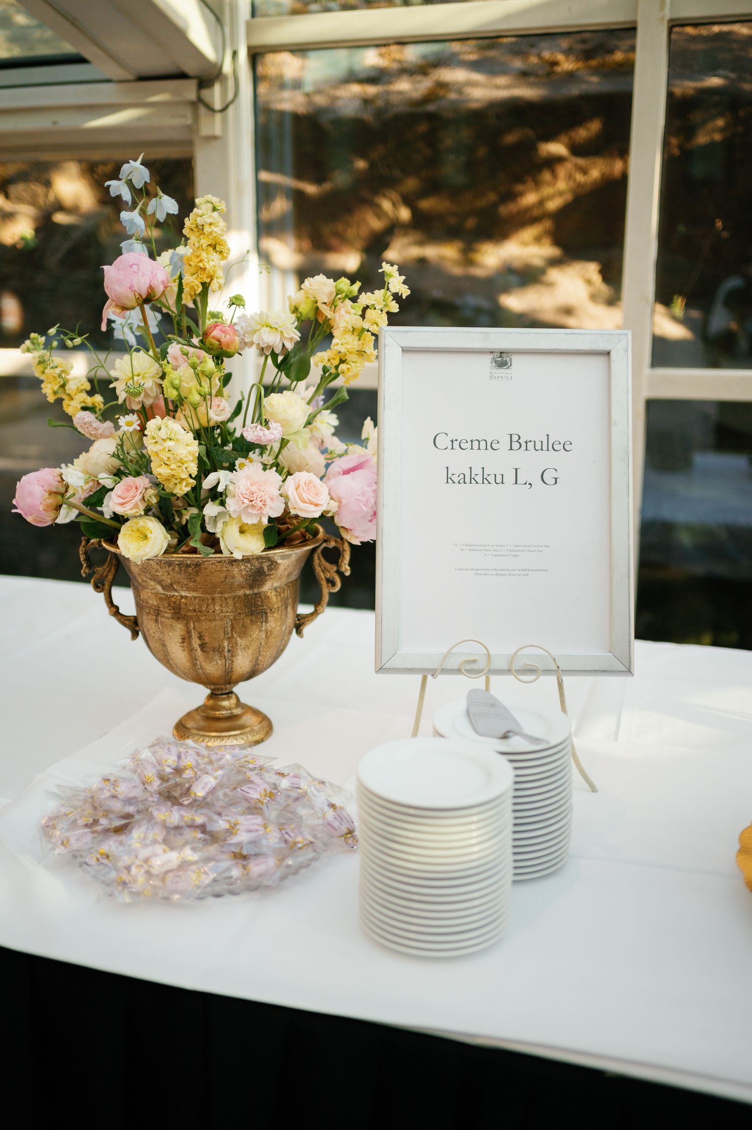 Elegant wedding dessert table with gold urn floral arrangement, Creme Brulee cake sign, and striped plates.