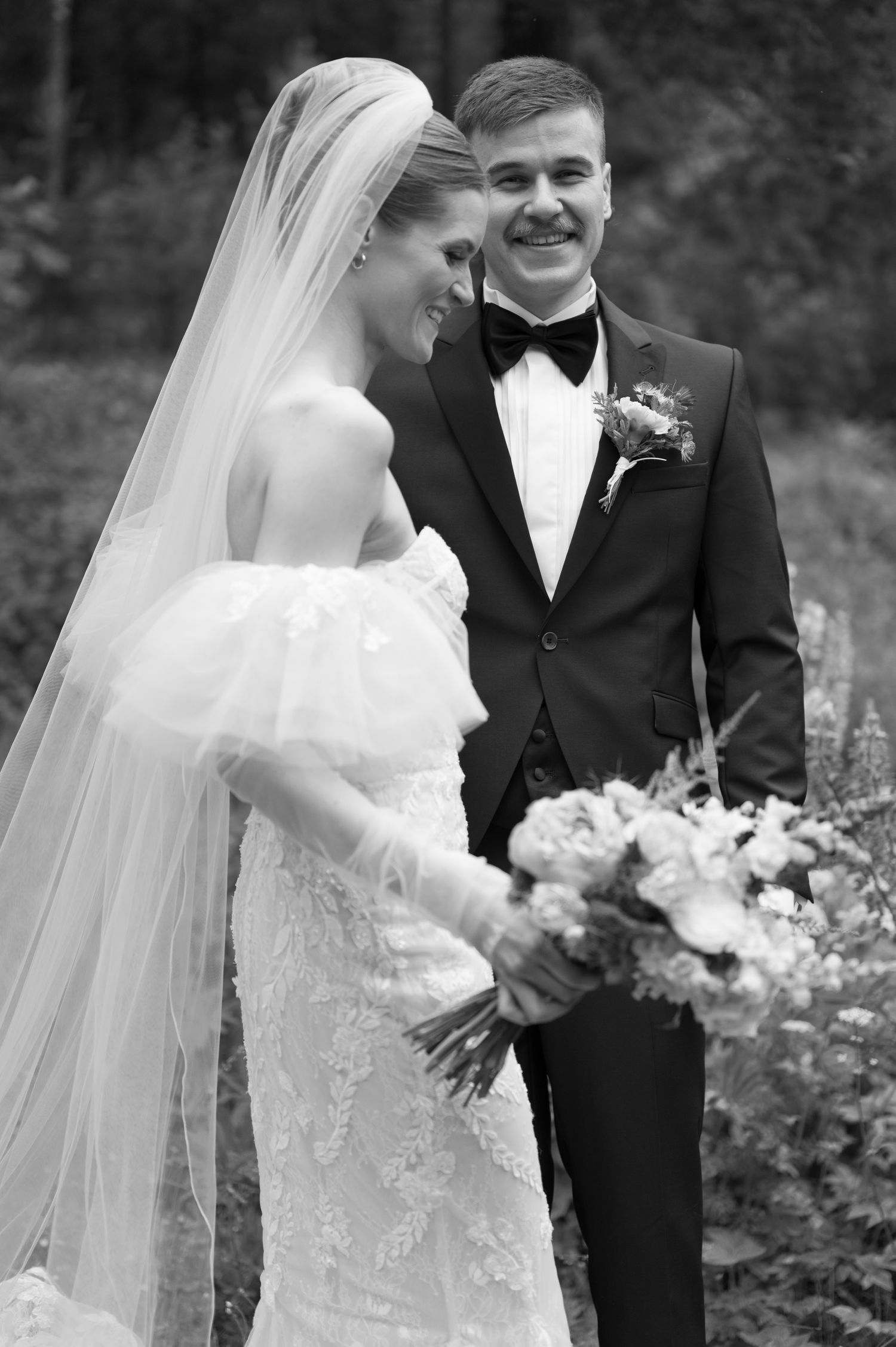 Black and white portrait of a joyful wedding couple sharing an intimate moment outdoors.