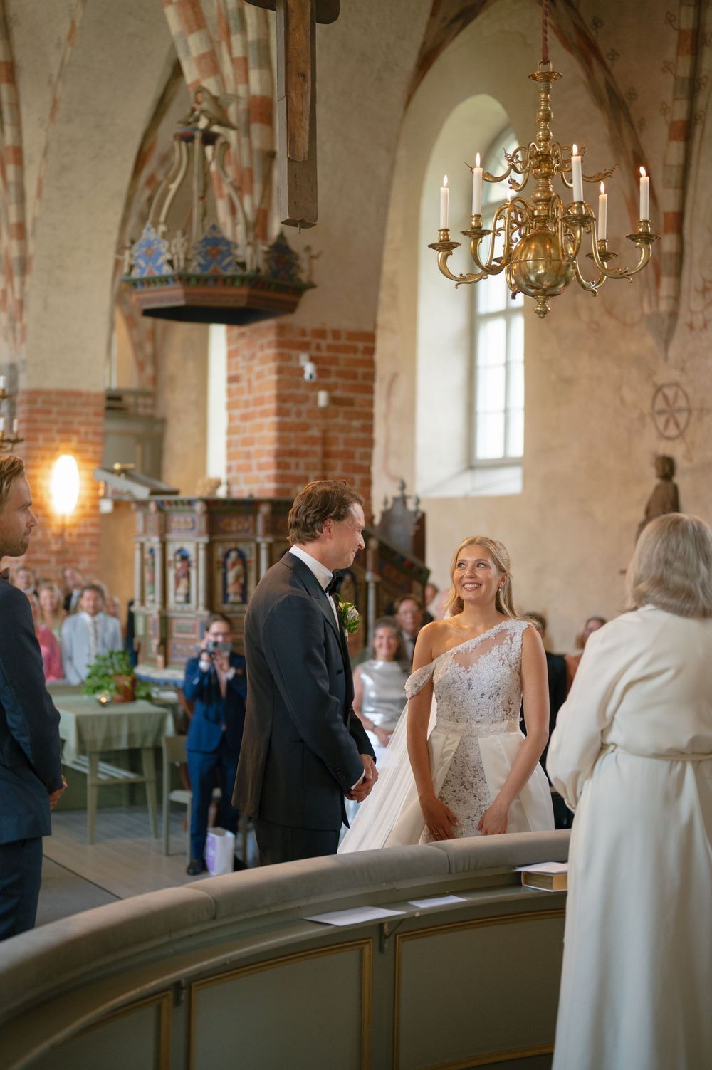 A wedding ceremony takes place in a historic church with exposed brick walls and elegant chandeliers.