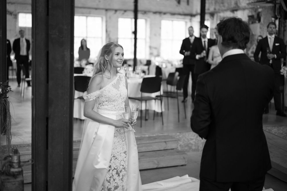 Wedding reception crowd watching speeches in an industrial space with exposed structural elements.