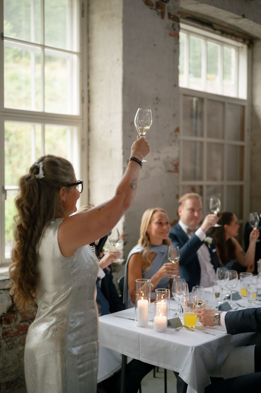 Wedding guests raising glasses for a toast at long dining tables.