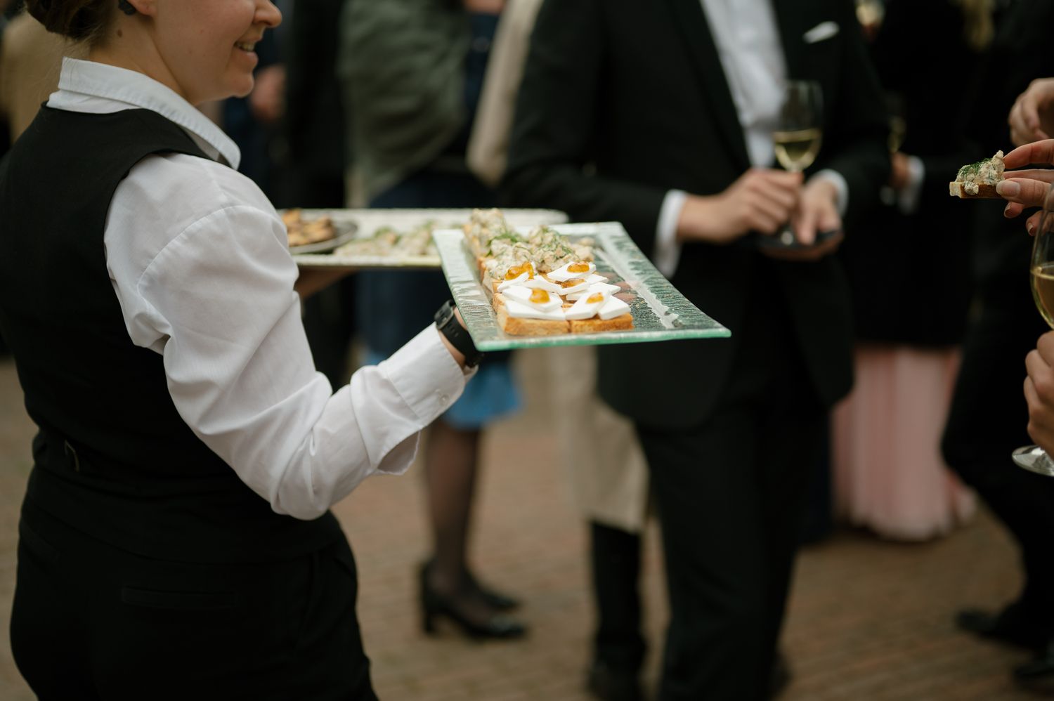 Catering staff serve appetizers on silver platters at an elegant cocktail reception.
