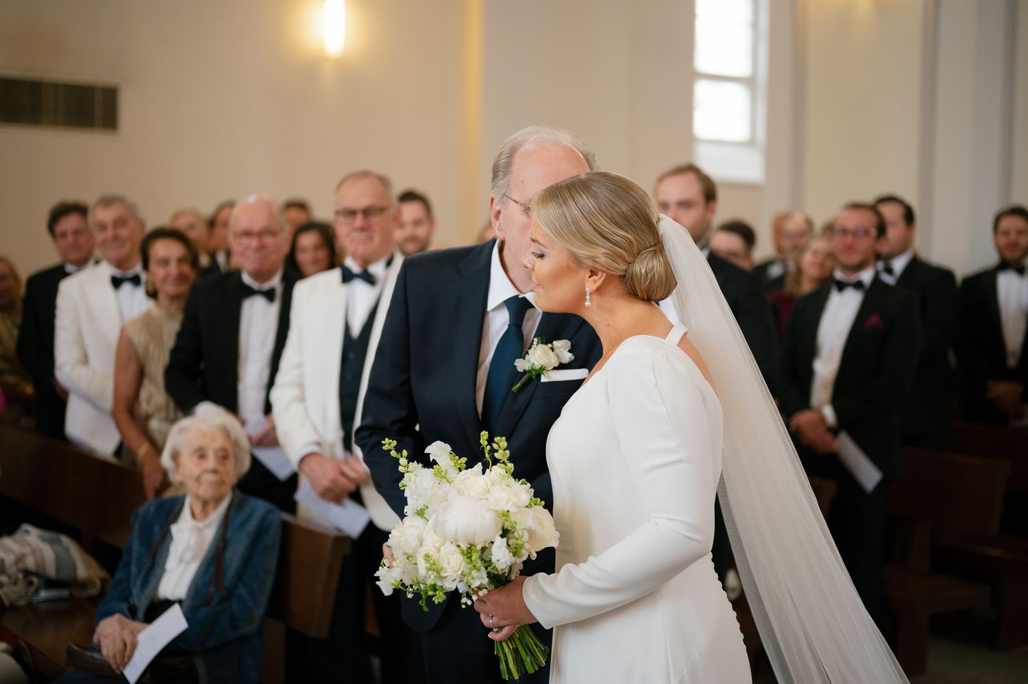 A joyful wedding ceremony moment captured in a bright church with guests looking on as the couple embraces.