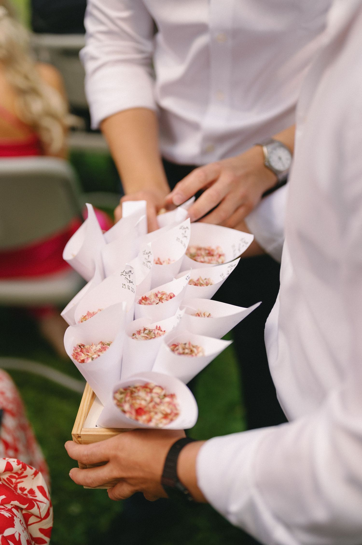 Server holding small paper cups with appetizers at an outdoor wedding reception.