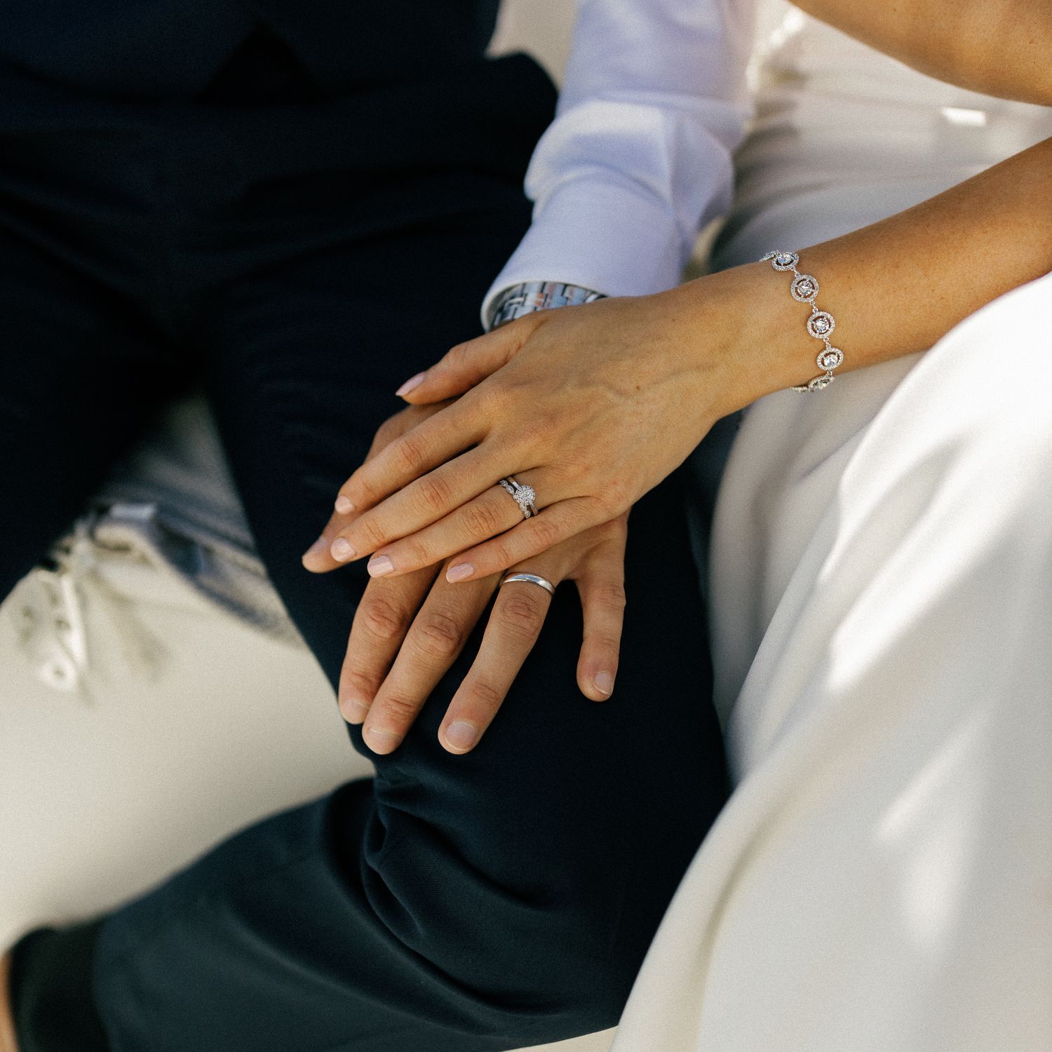 Close-up detail of hands and wedding attire against dark fabric.