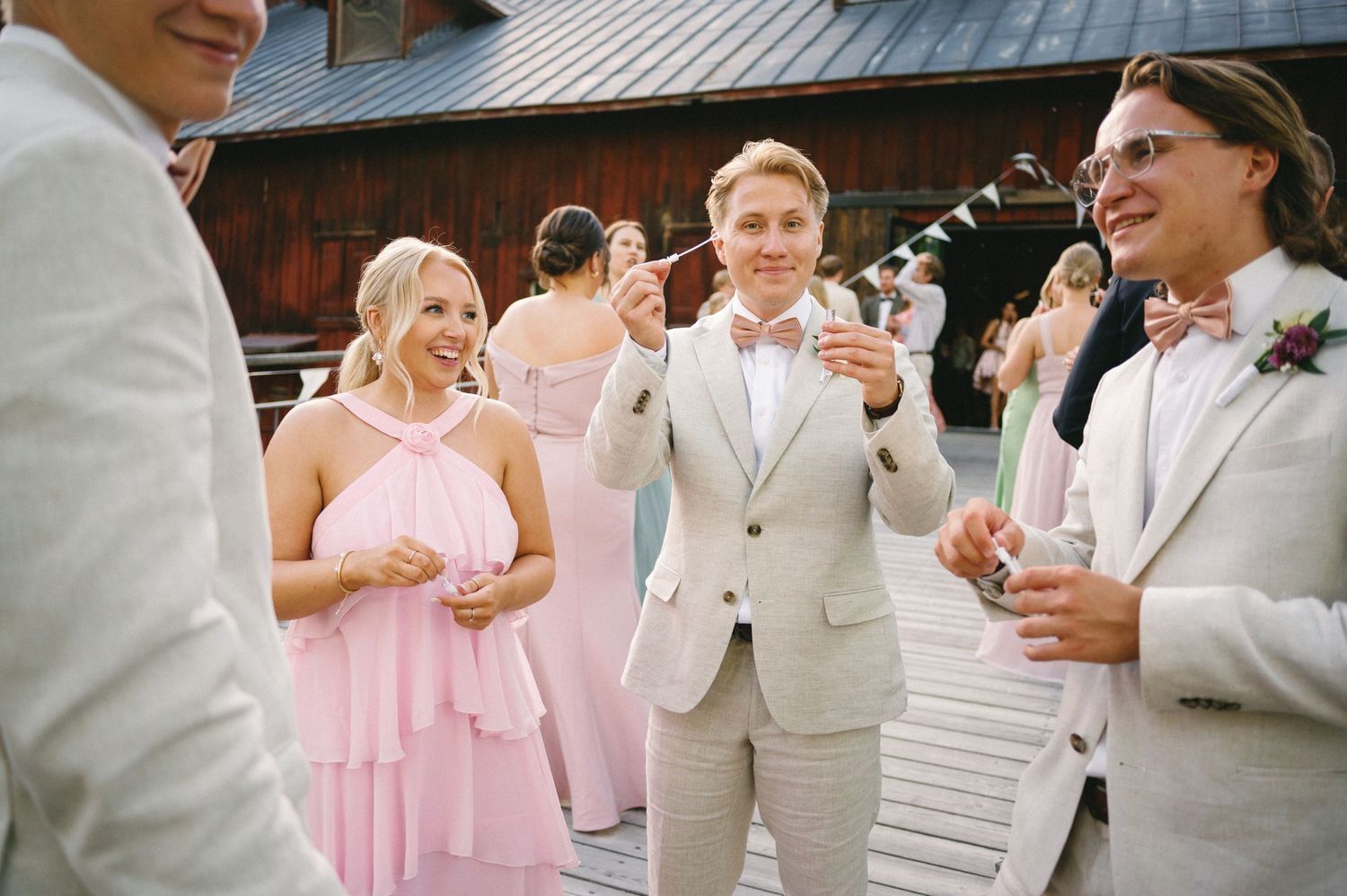 Wedding party members in light colored attire socializing during outdoor reception.