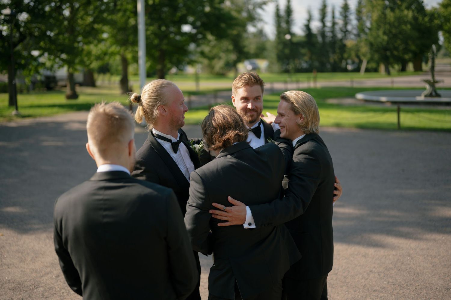 Groomsmen in black tuxedos gather together during wedding celebrations.