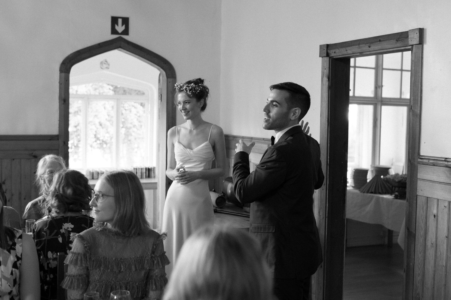 Black and white photograph of people gathered by windows in an indoor venue.