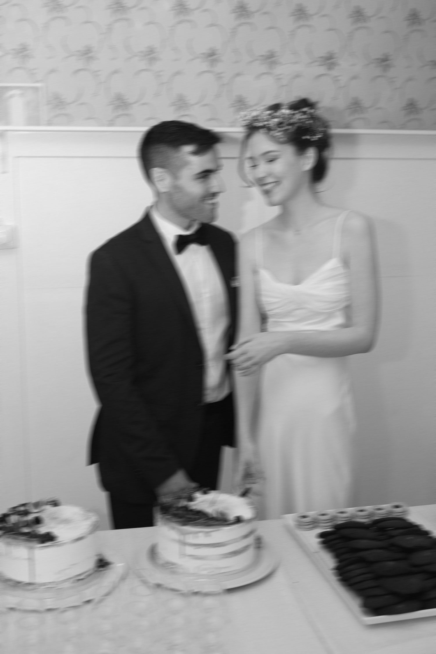 Black and white photo of a couple laughing while cutting their wedding cake.