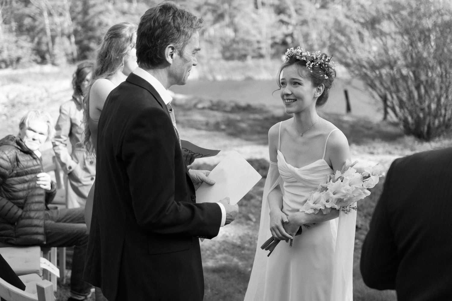 A black and white photo of a joyful wedding ceremony exchange between couple outdoors.
